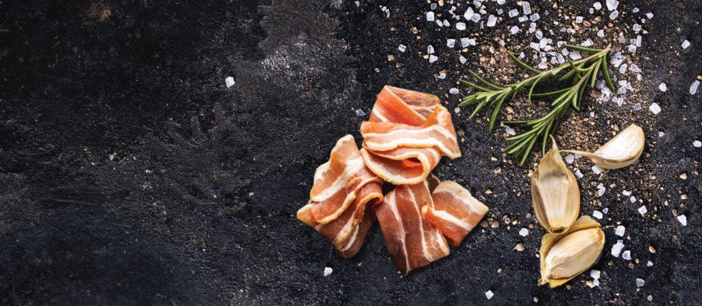 Bacon rashers with rosemary, garlic and sea salt on dark stone