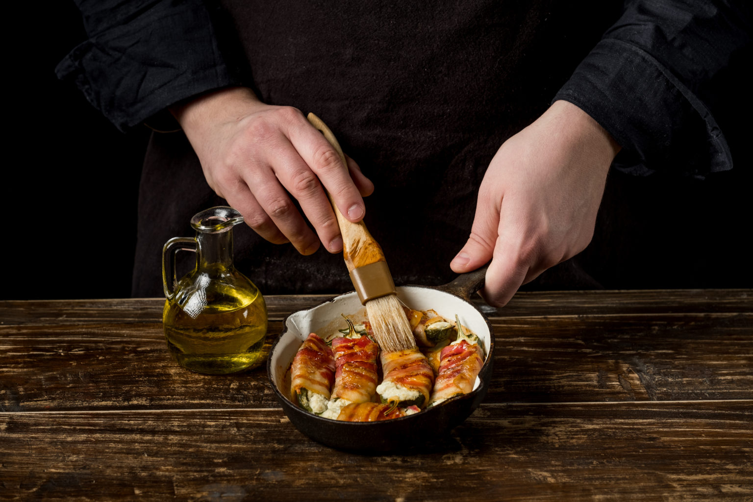 A chef basting bacon-wrapped rolls in a cast iron pan