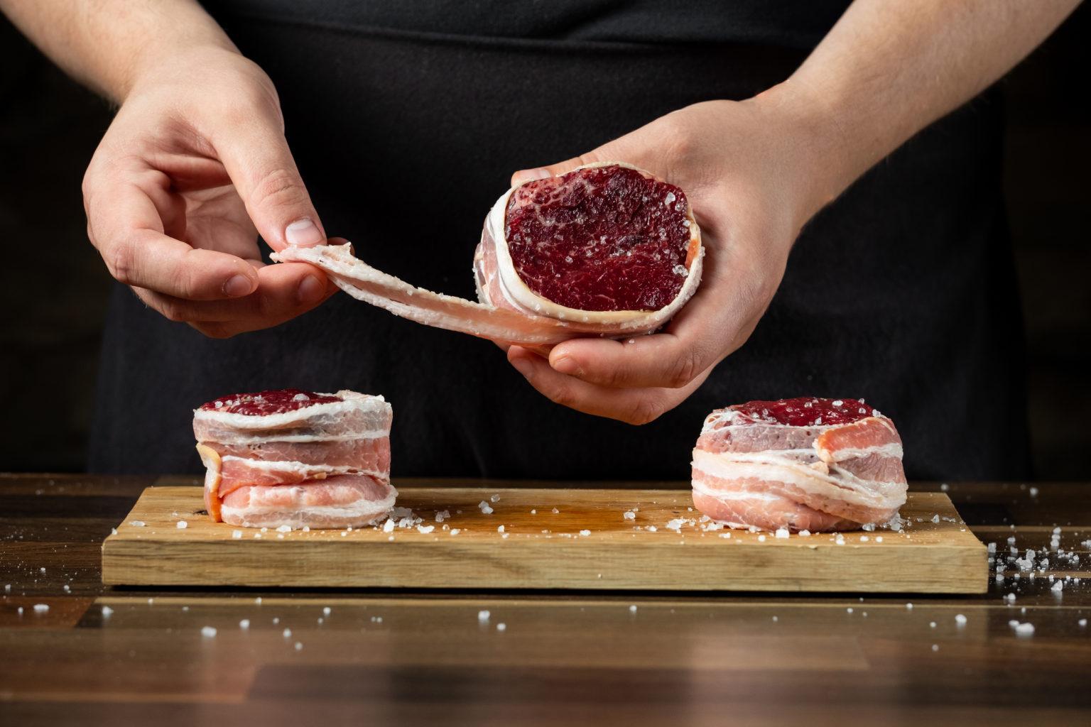 Hands wrapping fillet medallions in Creekside Farm bacon on a wooden board