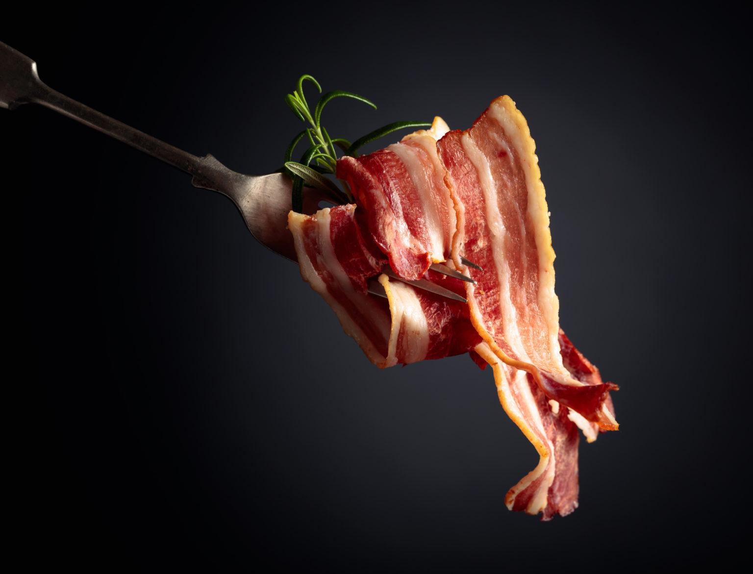 Rashers of Creekside Farm bacon draped over a fork with rosemary